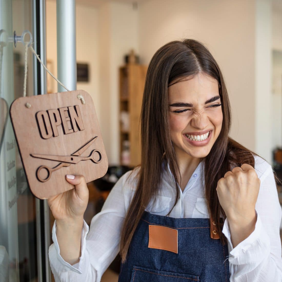 A South African salon owner smiling and holding an open for business sign